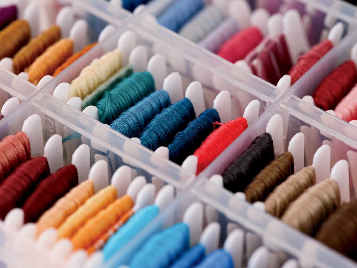 Bobbins With Different Colour Embroidery Threads In A Plastic Sorting Box. Close Up